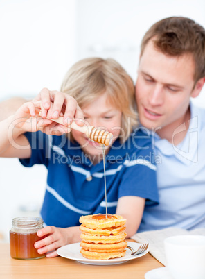 Smiling boy and his father putting honey on waffles