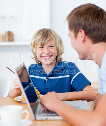 Smiling boy having breakfast while his father using a laptop