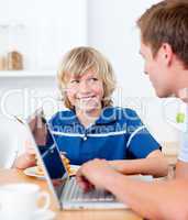 Cute boy having breakfast while his father using a laptop