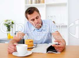 Concentrated man reading a newspaper while having breakfast