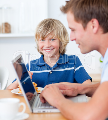 Adorable boy having breakfast while his father using a laptop