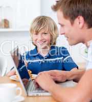 Adorable boy having breakfast while his father using a laptop