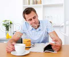 Smiling man reading a newspaper while having breakfast