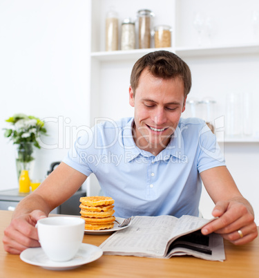 Cheerful man reading a newspaper while having breakfast