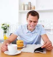 Cheerful man reading a newspaper while having breakfast