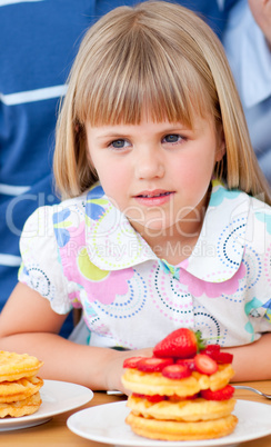 Cute little girl eating waffles with strawberries