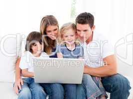 Portrait of a jolly family using a laptop sitting on sofa