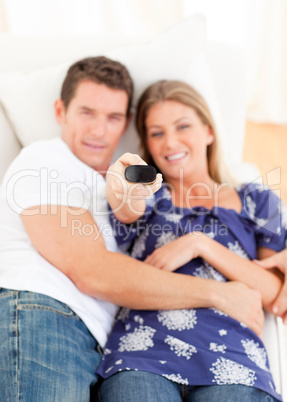Smiling lovers watching television lying on sofa
