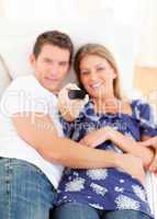 Smiling lovers watching television lying on sofa