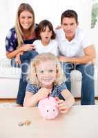 Blond little girl inserting coin in a piggybank