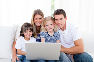 Portrait of a joyful family using a laptop sitting on sofa