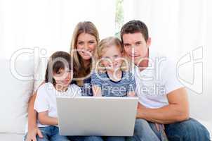 Portrait of a joyful family using a laptop sitting on sofa