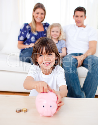 Cheerful little boy inserting coin in a piggybank
