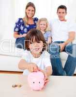 Cheerful little boy inserting coin in a piggybank