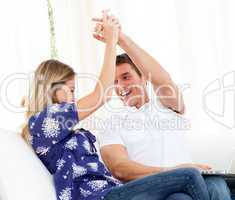 Mirthful couple using a laptop sitting on sofa