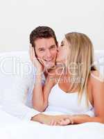 Intimate woman kissing her husband sitting on bed