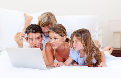 Merry family buying online lying down on bed