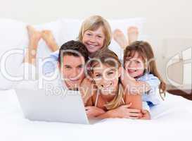 Smiling family looking at a laptop lying down on bed