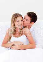 Affectionate man kissing his wife sitting on bed