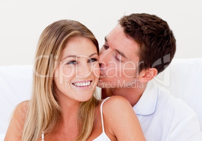 Portrait of an ffectionate man kissing his wife sitting on bed