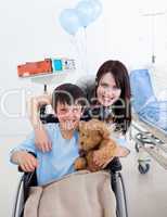 Smiling little boy sitting on wheelchair and his mother