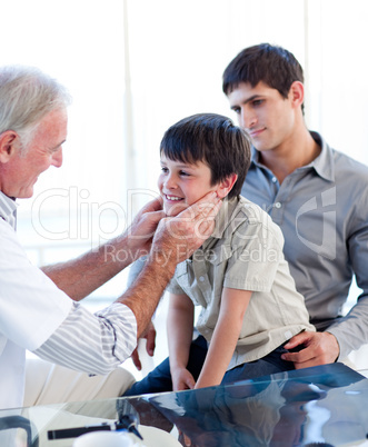Senior doctor examing little boy throat with his father