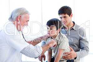 Senior doctor examining a little boy with his father