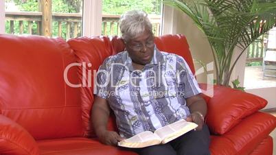 Senior woman reads bible on sofa - 2