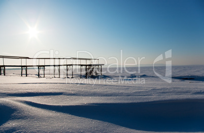 Wooden bridge on snowy coast of river, in early morning