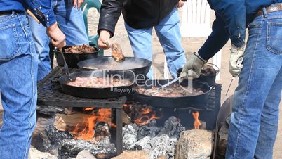 Men cooking steaks over fire