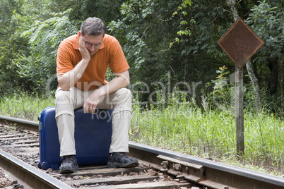 Mann sitzt auf Koffer auf Gleisen