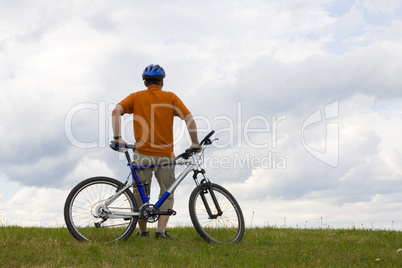 Mann steht mit Mountainbike auf Wiese