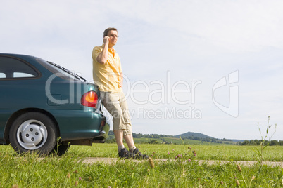 Mann telefoniert neben seinem Auto
