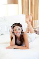 Pretty woman lying down on bed listening music