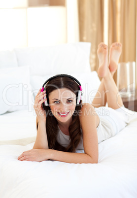 Smiling woman lying down on bed listening music