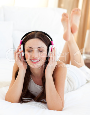 Attractive woman lying down on bed listening music