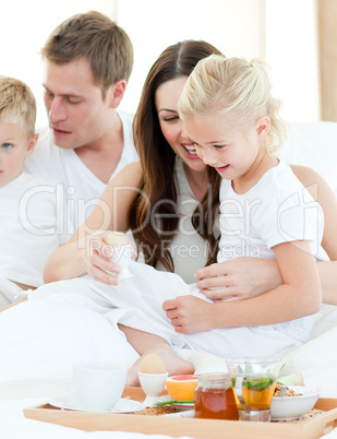 Elated family having breakfast sitting on bed