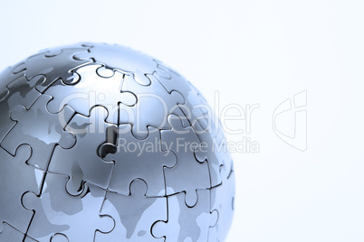 Metal puzzle globe isolated on white background, close-up in blue light