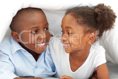 Portrait of laughing siblings lying down on bed