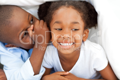 Ethnic little boy whispering something to his sister