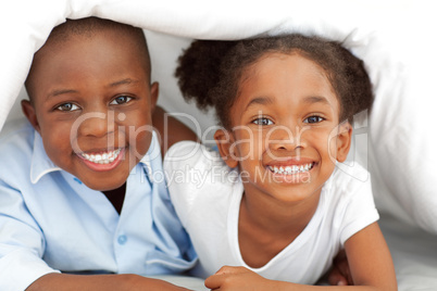 Portrait of ethnic siblings lying down on bed
