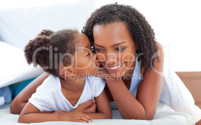 Cute little girl woman kissing her mother lying down on bed