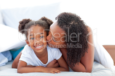 Loving woman kissing her daughter lying down on bed