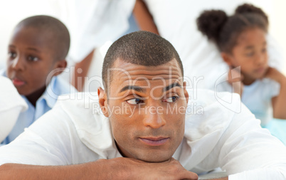 Portrait of a relaxed man lying down on bed with his children