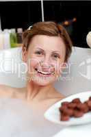 Radiant woman eating chocolate while having a bath