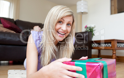 Joyful young woman holding presents lying on the floor