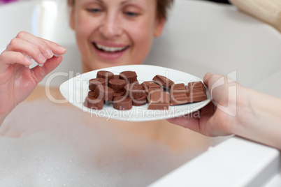 Cheerful young woman eating chocolate while having a bath