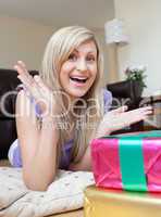 Astonished pretty woman opening gifts lying on the floor