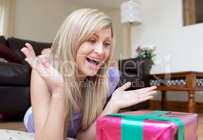Surprised young woman opening gifts lying on the floor