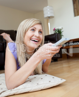 Laughing woman watching TV lying on the floor